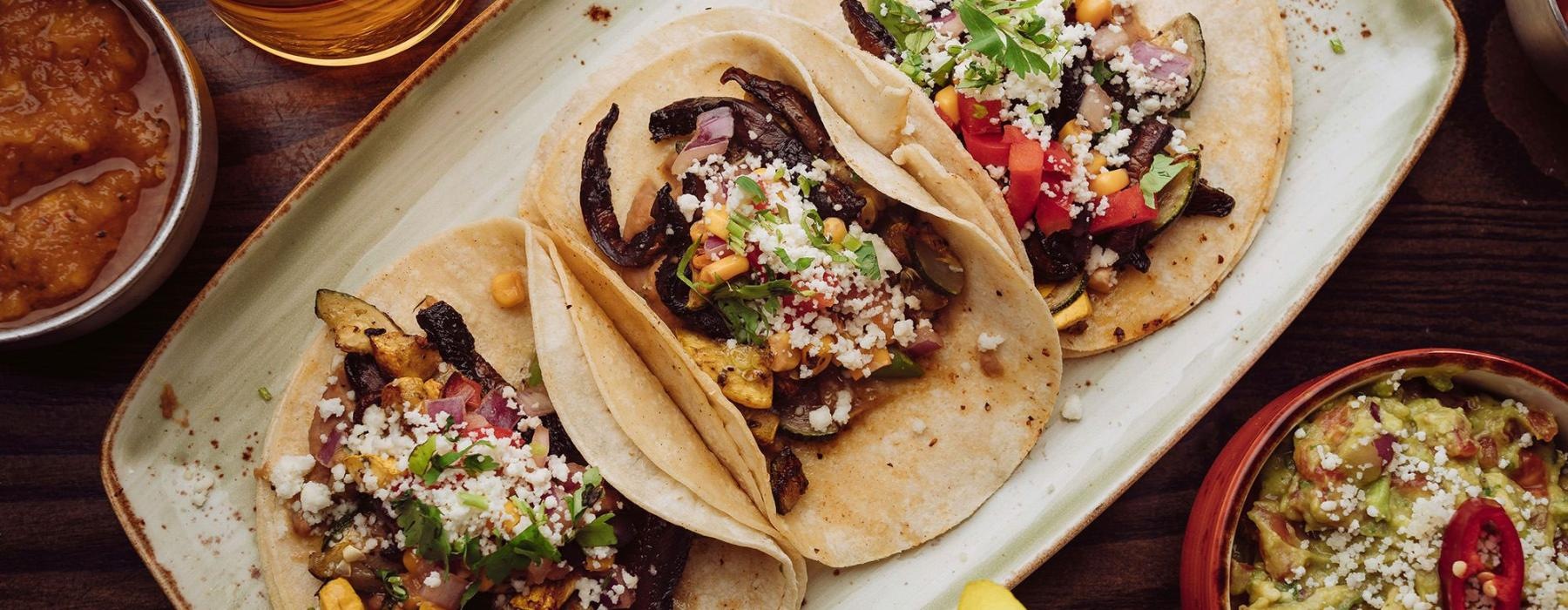 A plate with three tacos and a bowl of guacamole.